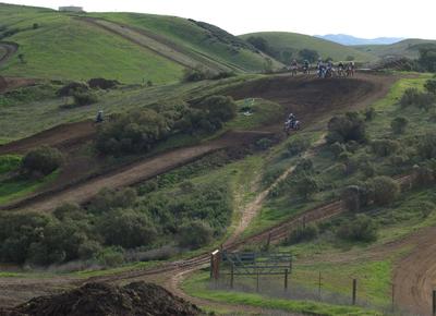motorcycle track with green hills background and several riders waiting to ride onto track thumbnail